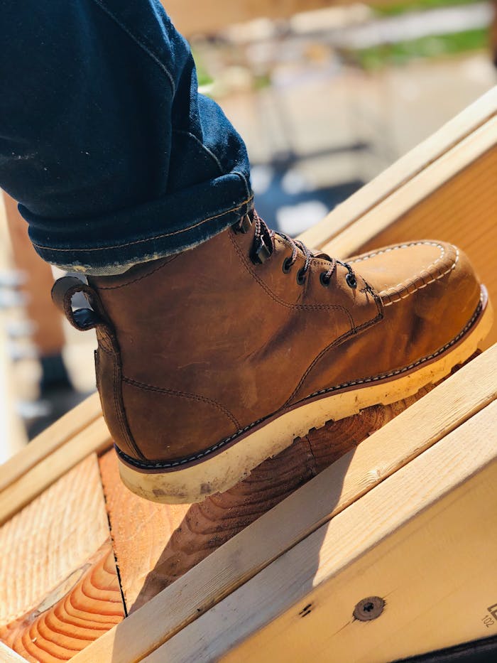 Close-up of a brown leather boot on wooden planks, showcasing rugged fashion and style.