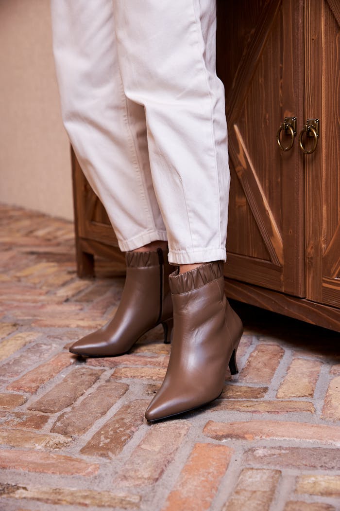 Fashion-forward brown ankle boots paired with white pants in an indoor setting.