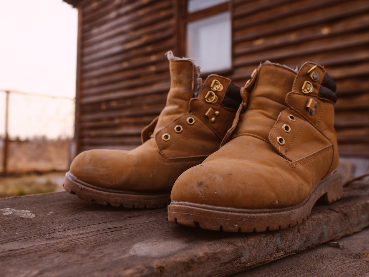 Close-up of rugged suede boots resting outside a rustic wooden cabin on a wooden platform.
