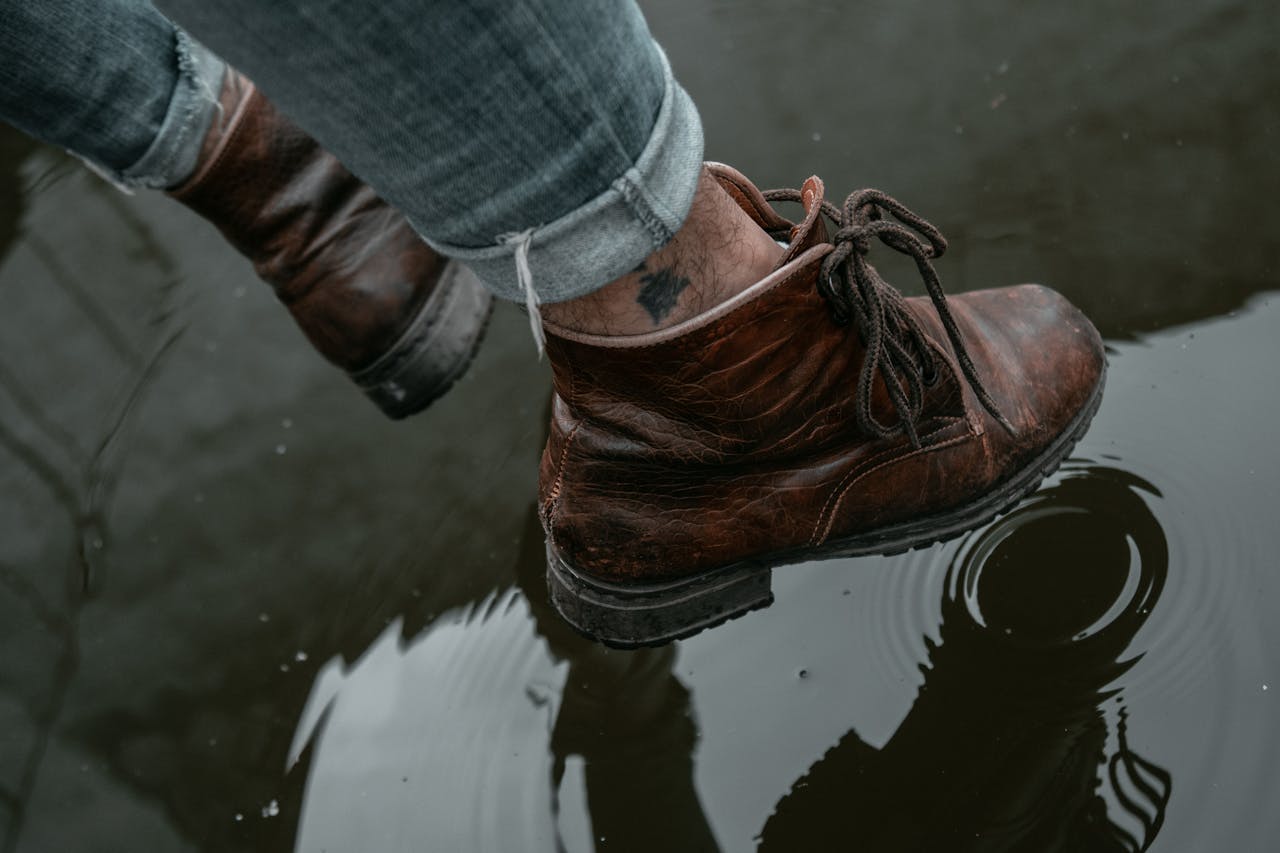 Brown leather boots stepping in a puddle with clear water reflection.
