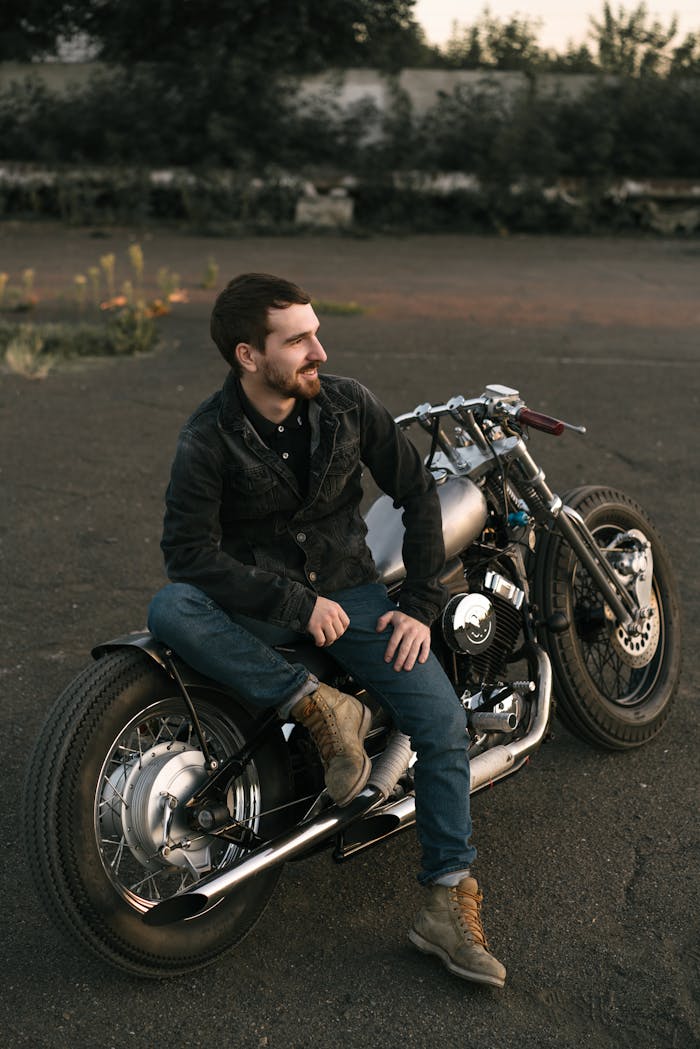 A man sitting proudly on a custom motorcycle in an outdoor setting. Ideal for lifestyle and adventure themes.