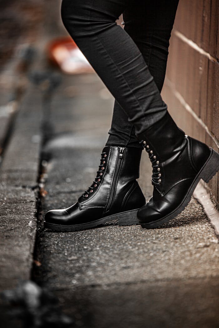 Close-up of black leather boots and legs on urban pavement, showcasing fashion in focus.