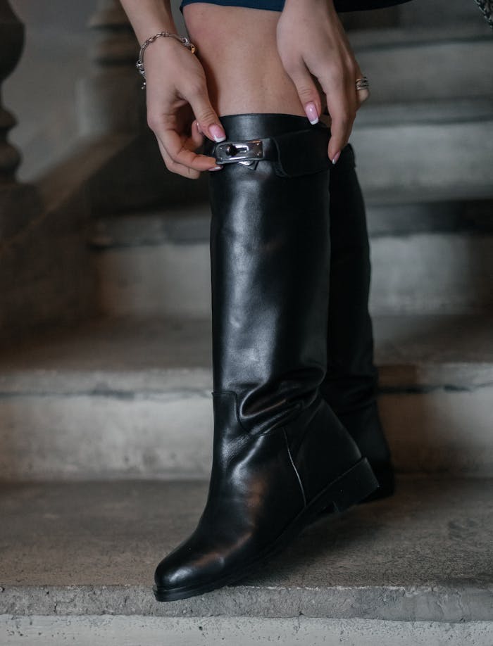 Elegant black leather boots with hands adjusting strap, captured on stone steps.